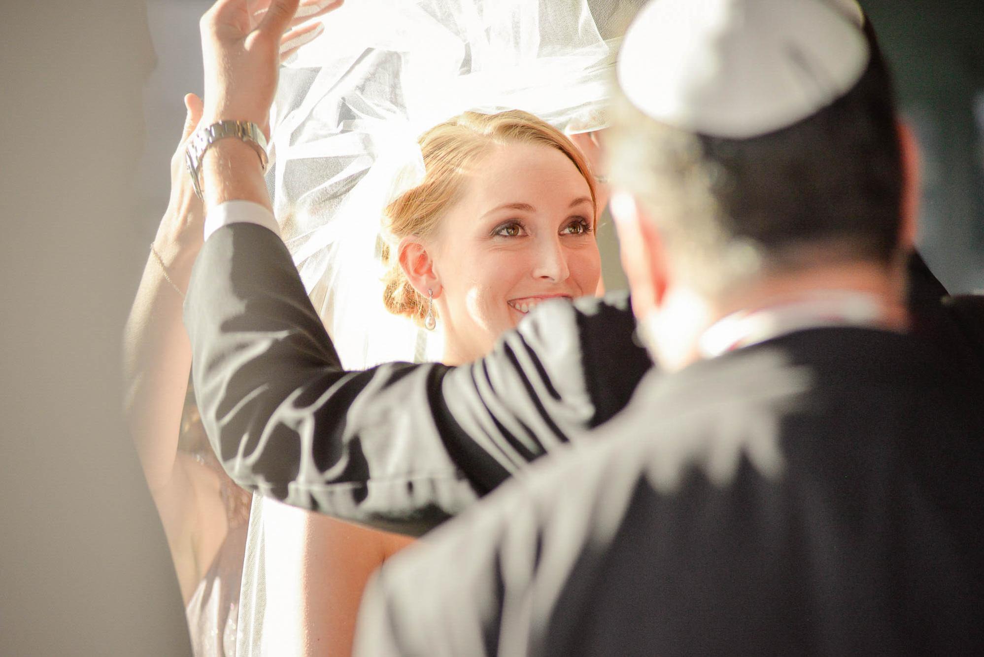 Bride smiling as her veil is lifted over her face during a ceremony