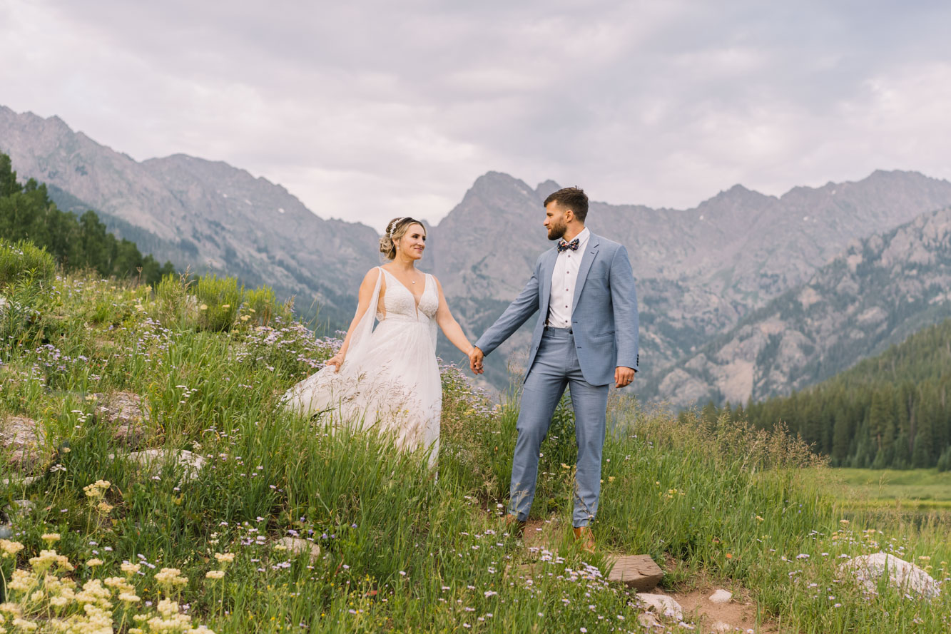 Bride and groom holding hands in a wildflower meadow with Colorado mountain peaks behind them